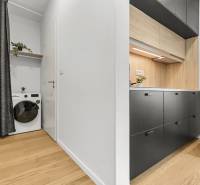 The kitchen in a studio apartment with a wood-patterned floor and a washing machine with a shelf.