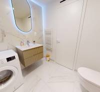 A bathroom in a studio apartment with a washing machine, a sink, and ceramic tiles.