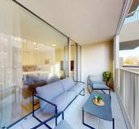 A balcony with seating, a view of the surrounding buildings, glass doors to a studio apartment.