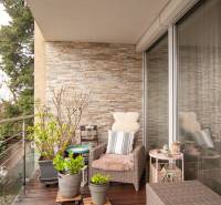 Balcony of a 2-room apartment with comfortable seating, flower pots, and glass doors.