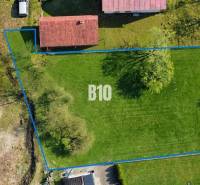 A plot for living in Raková with green grass and trees bordered by a blue line.