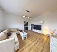 Living room with wood-patterned flooring in a three-room apartment with a light-colored sofa and a TV cabinet.