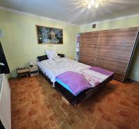 Bedroom in a family house with a bed, wardrobe, and wooden decor flooring.