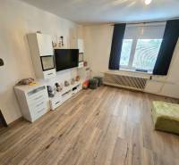 Living room in a family house with a television, white furniture, and a wooden decor floor.