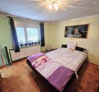 A bedroom in a family house with a bed, green walls, and a floor with a wooden decor.
