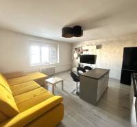 Living room with a large yellow sofa, kitchen island, and television in a 2-room apartment.