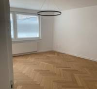 A room in a 2-room apartment with a wood-patterned floor and a window.