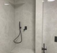 A shower corner in a 2-room apartment with a black faucet and a stone wall.