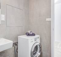 A bathroom with light tiles, a sink, and a washing machine next to the toilet in a 2-room apartment.