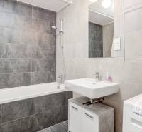 A bathroom with a bathtub, sink, and washing machine in a 2-room apartment.