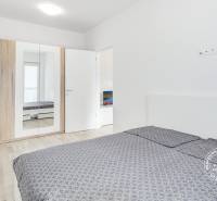 A bedroom with wood-patterned flooring, a wardrobe, and a bed in a two-room apartment.
