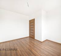 An empty room in a family house with white walls and a wood-patterned floor.