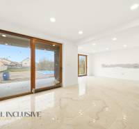 A spacious interior of a family house with large windows and a view of the garden with a swimming pool.