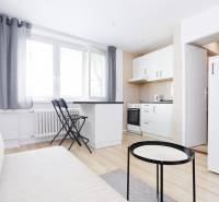 A kitchen in a 2-room apartment with white furniture and a wooden decor floor.