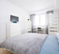 Bright bedroom with a bed, mirror, dresser, and wood-patterned floor.
