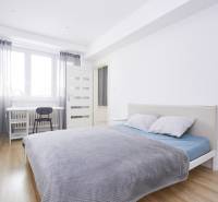 Bright bedroom in a two-room apartment with a desk and wood-decorated flooring.
