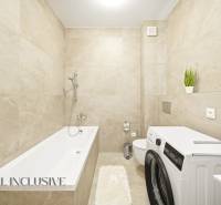 A bathroom with light tiles, a bathtub, a washing machine, and decorative plants in a 4-room apartment.