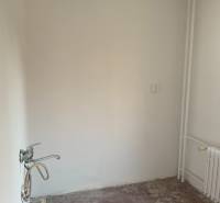 An empty room in a two-room apartment without flooring and with a sink.