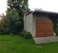 A garage in a family house on a street in Blatnica, surrounded by greenery and climbing plants.