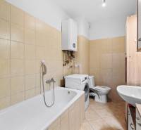 Bathroom with shower, washing machine, and sink in a 2-room apartment with beige tiles.