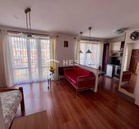 Interior of a 1-room apartment with wooden flooring, a kitchen, light curtains, and comfortable seating.