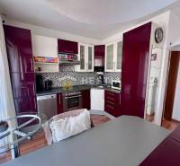 A kitchen with burgundy cabinets in a studio apartment, decorative mosaic tiles on the wall.