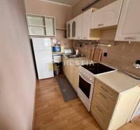 A kitchen in a 2-room apartment with a wooden decor floor and light cabinets.