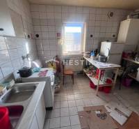 A kitchen with a tiled floor, a stove, and dishes on the shelf, catering spaces.