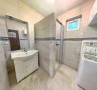 A bathroom in a family house with a shower, washing machine, tiled walls, and a sink.
