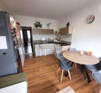 A kitchen of a three-room apartment with a wooden decor floor, a dining table, and appliances.