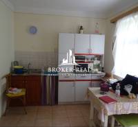 A kitchen in a family house with white furniture and a table with a plastic tablecloth.