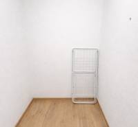 A white room in a two-room apartment with a wood-patterned floor and a drying rack.