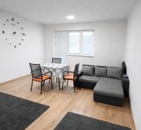 Living room in a two-room apartment with a sofa, table, and wooden decor flooring.
