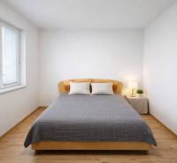 A bright bedroom with wood-patterned flooring in a 2-room apartment, decorated with a bed and a lamp.