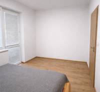 A bedroom in a two-room apartment with a wooden decor floor and a large window.