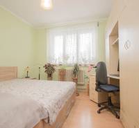 A bedroom in a family house with a wood-patterned floor, a bed, and a desk.