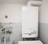 A bathroom with a gas boiler and shelves for cosmetics in a family house.