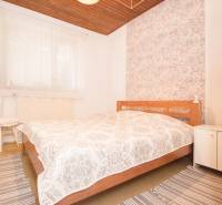 A bedroom in a family house with a wooden ceiling, decorative wallpaper, and striped carpets.