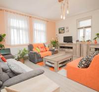 A living room in a family house with orange sofas, plants, and a wooden decor floor.