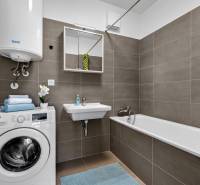A bathroom in a 2-room apartment with a washing machine, bathtub, sink, and gas boiler.