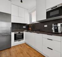 A kitchen in a 2-room apartment with a wood-patterned floor, white cabinets, appliances.