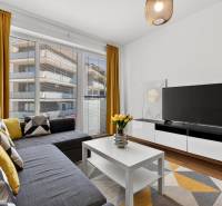 A two-room apartment with large windows, a sofa, a television, yellow curtains, and a wooden decor floor.