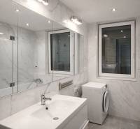Bathroom in a 2-room apartment with a bathtub, sink, and washing machine, with marble-look tiles.