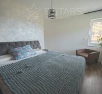 A bedroom in a family house with a bed with a textile headboard and a floor with a wooden decor.