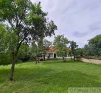 A family house in Dobroč with a spacious garden, surrounded by trees and a stone fence.