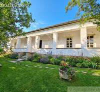 A family house in Dobroč with a garden and flower beds, lined with trees and a bench.