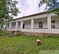 A family house in Dobroč, white facade, stone foundation, surrounded by greenery and trees.