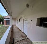 The veranda of a family house in Mužla with a white facade and a grassy yard.