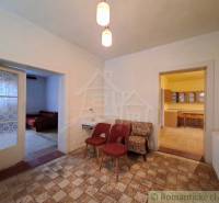 Interior of a family house with armchairs, a sink, a kitchen, and two open doors.