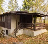 A wooden cabin on recreational land in Holčíkovce, surrounded by trees and fallen leaves.
